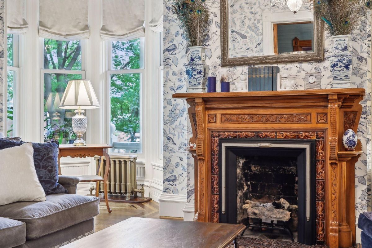 A detailed fireplace mantel is the focal point of this room, which also features bay windows and patterned wallpaper.