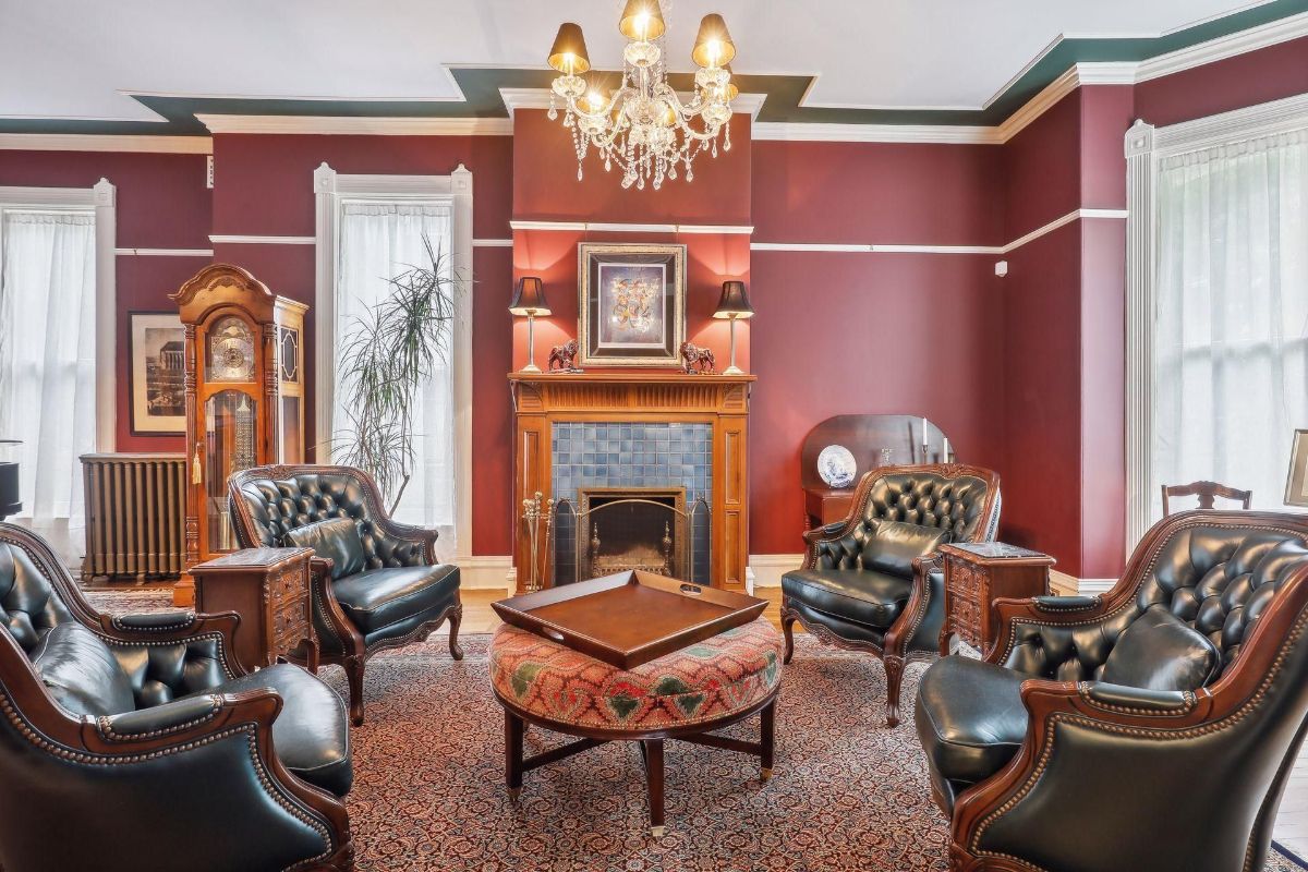 A richly decorated room features dark-wood furniture, including several armchairs arranged around a coffee table, and a fireplace.