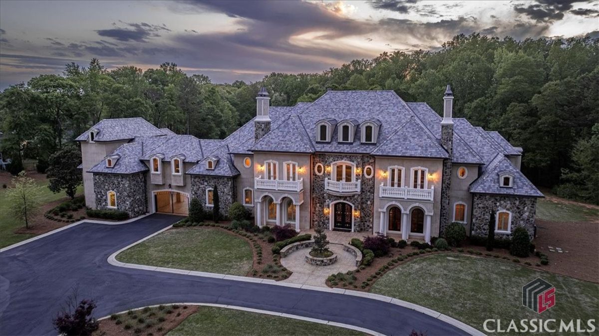 A stately French-inspired estate showcases timeless architecture with stone accents, elegant balconies, and glowing evening ambiance.