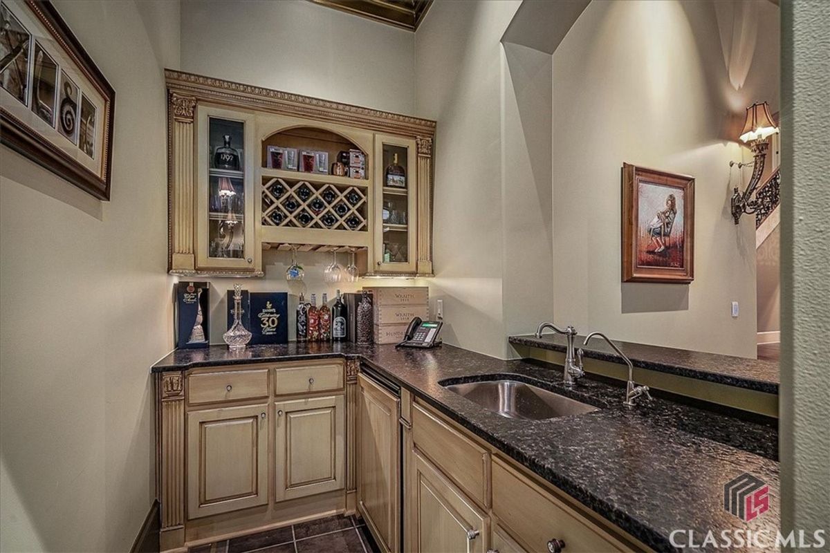 An elegant wet bar features detailed cream cabinetry, a built-in wine rack, glass-front displays, and granite countertops, perfect for entertaining.