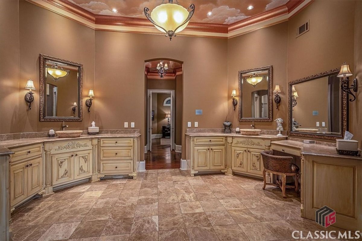 An opulent bathroom showcases dual vanities with ornate cabinetry, a makeup station, and a tray ceiling adorned with a cloud mural.