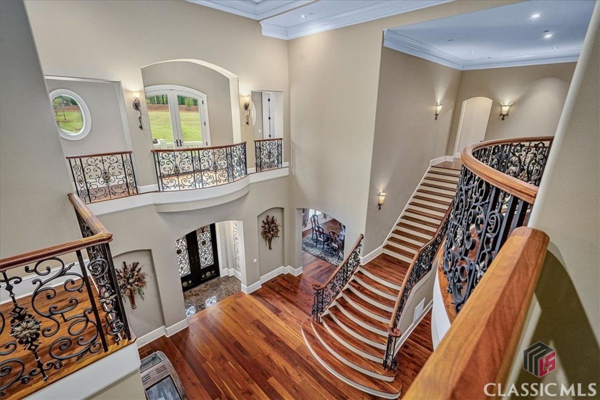 A grand staircase adorned with wrought iron balustrades leads to an upper gallery with elegant views of the open foyer and its double-door entry.