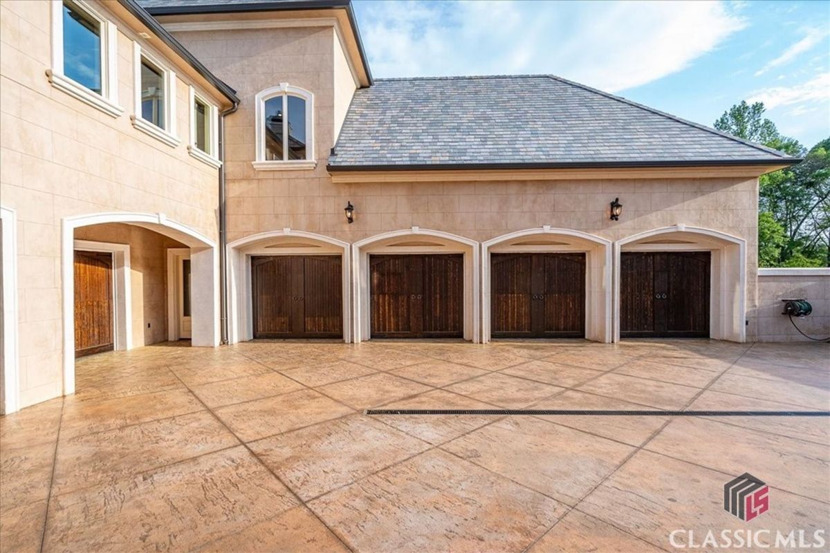 An expansive driveway leads to a four-car garage with arched wooden doors and a sleek, stone-accented exterior.