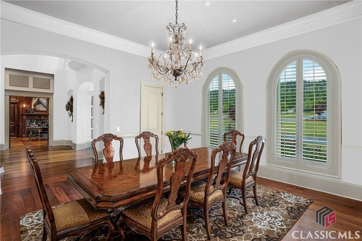 Dining room showcases a crystal chandelier, arched windows with plantation shutters, and a refined table with intricately carved chairs.