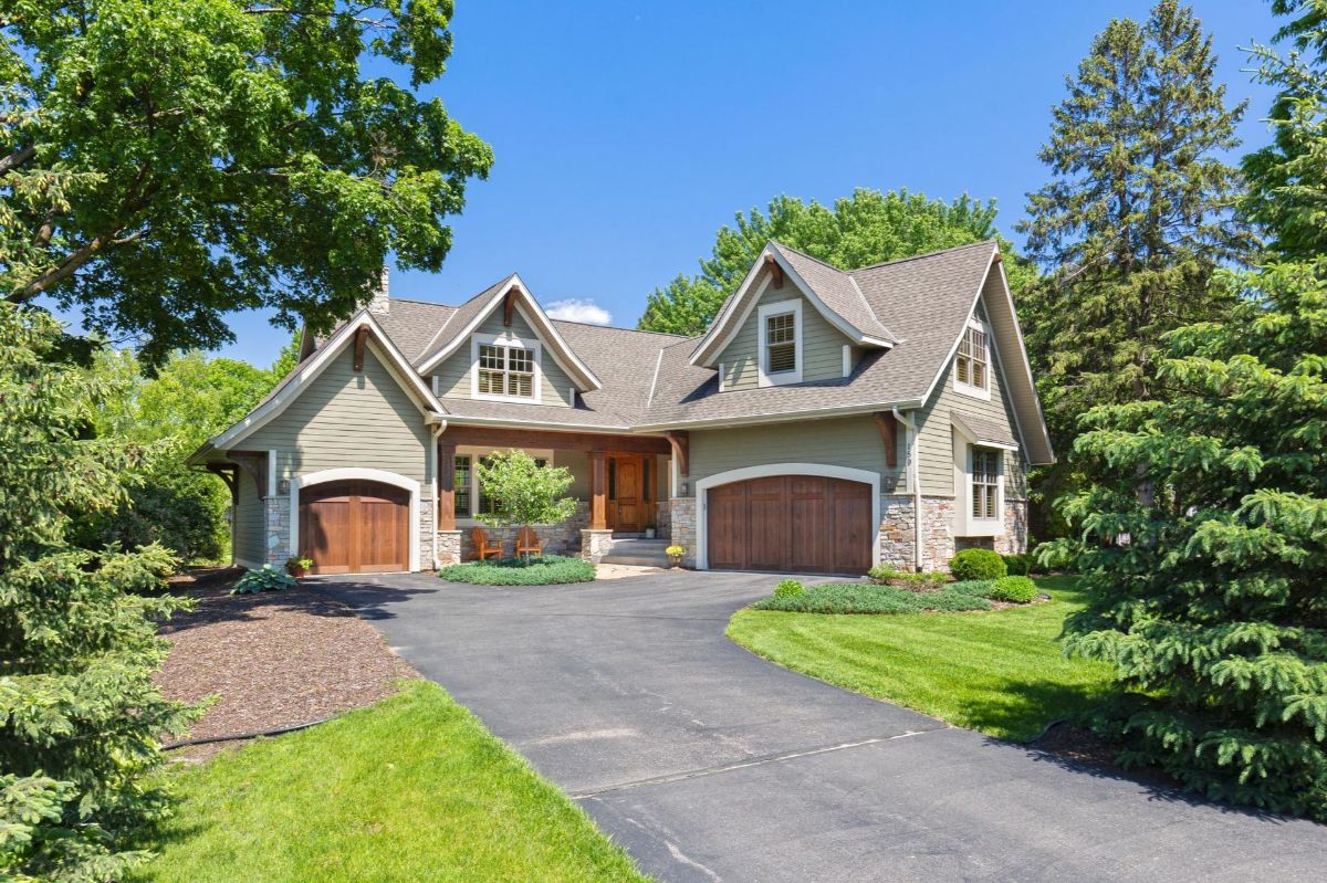 Charming craftsman-style home features a welcoming front porch, stone accents, and lush landscaping.