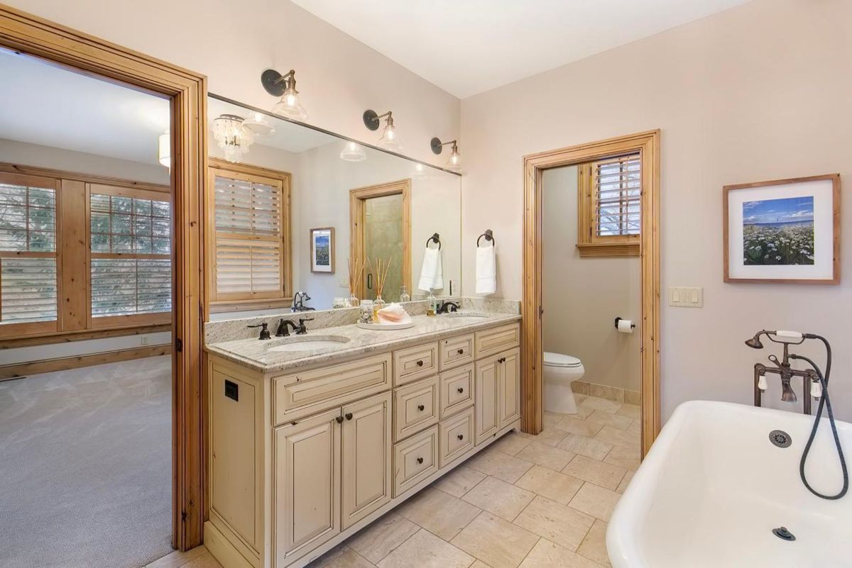 Elegant bathroom features a freestanding tub, double vanity with granite countertops, and warm wood accents.