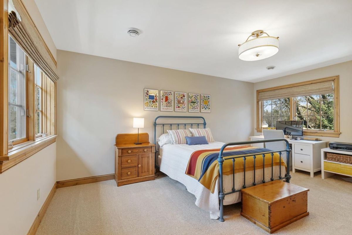 Bright bedroom combines colorful bedding, a vintage metal bed frame, and a functional workspace.