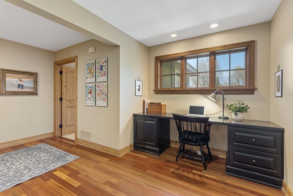 Compact home office features rich wood flooring, built-in black cabinetry, and a window with natural light.