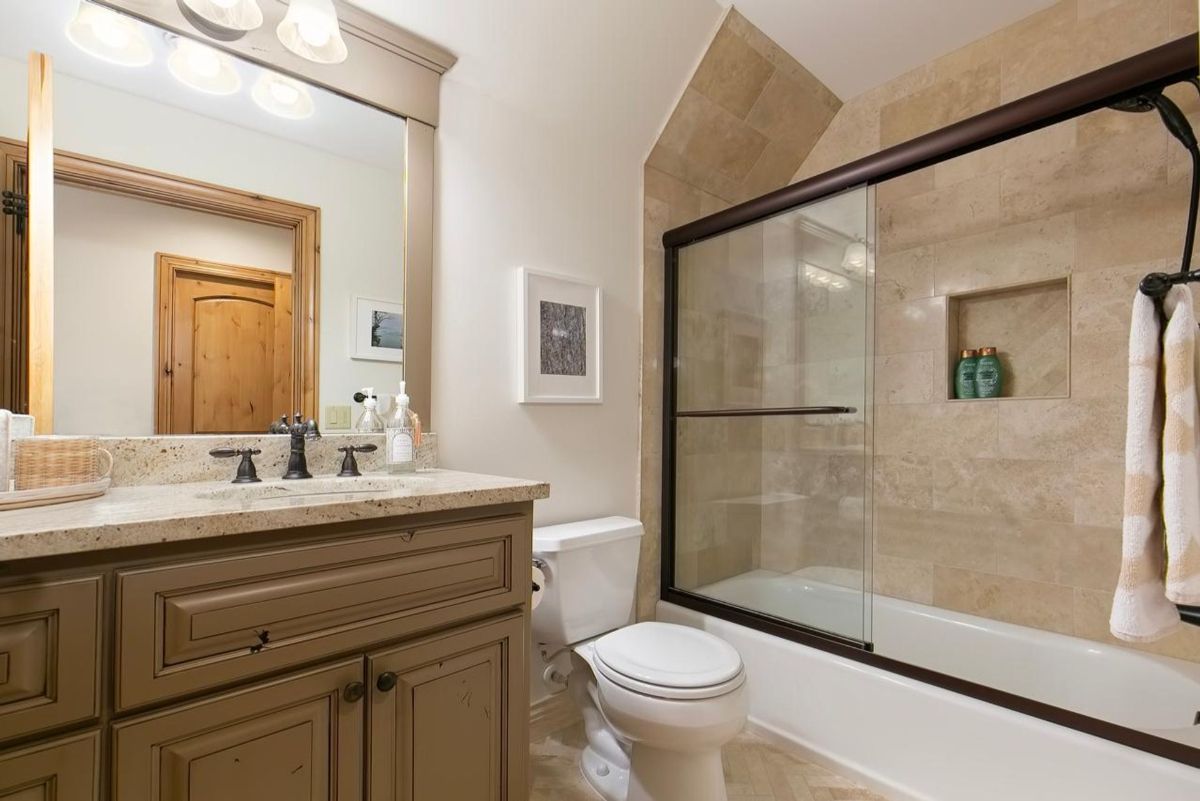 Charming bathroom includes a tiled shower-tub combination, granite vanity, and warm neutral tones.