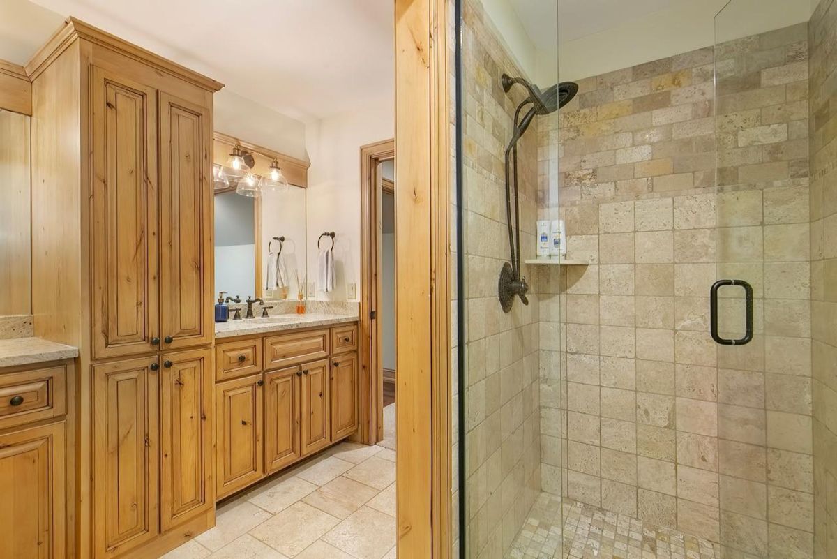 Rustic bathroom showcases custom wood cabinetry, a tiled walk-in shower, and elegant bronze fixtures.