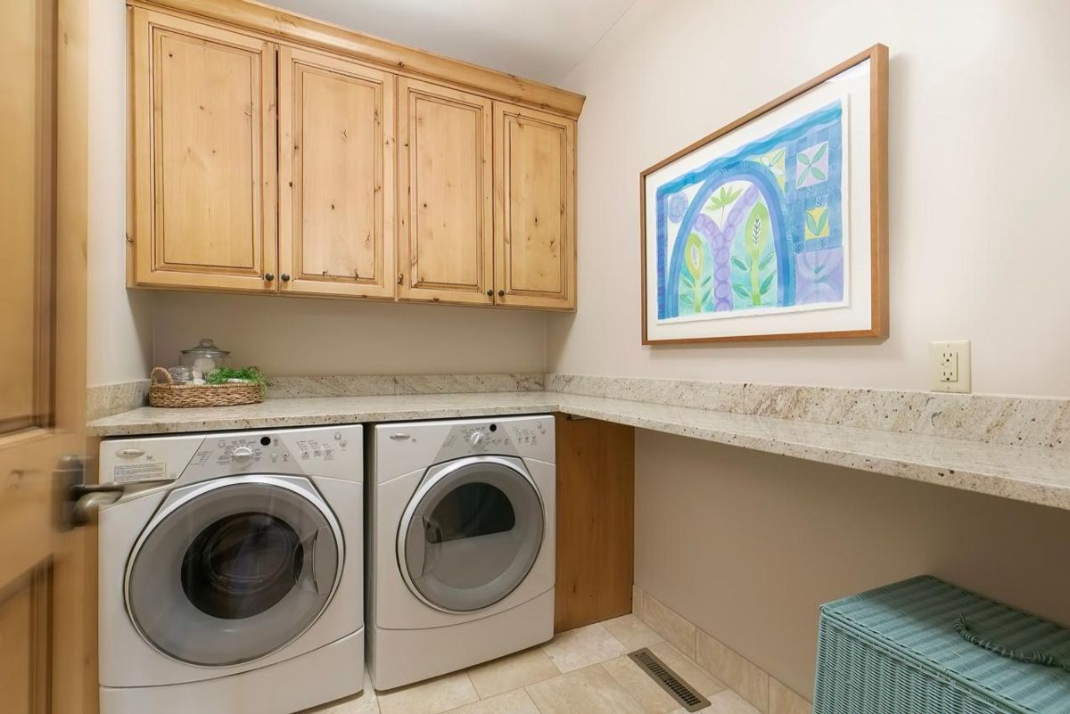 Efficient laundry room includes front-loading appliances, custom wood cabinetry, and granite countertops for a functional yet stylish workspace.