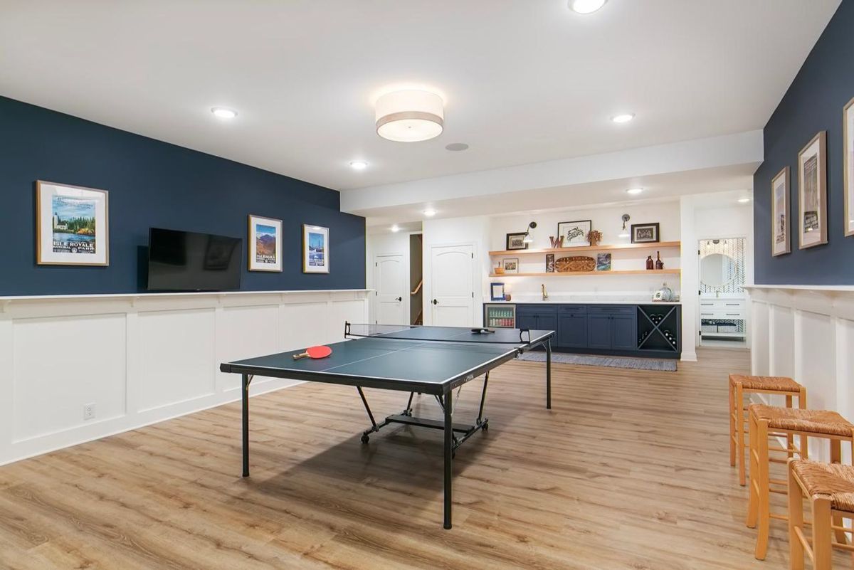 Spacious game room features a ping-pong table, custom navy cabinetry with open shelving, and vibrant wall art for a playful atmosphere.