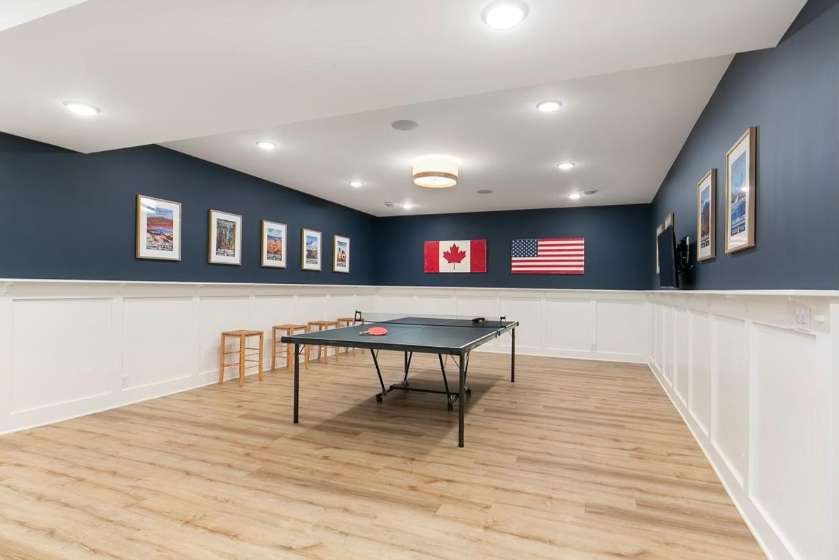 Game room combines functionality with flair, featuring flag wall art, custom wainscoting, and a ping-pong table on durable wood-look flooring.