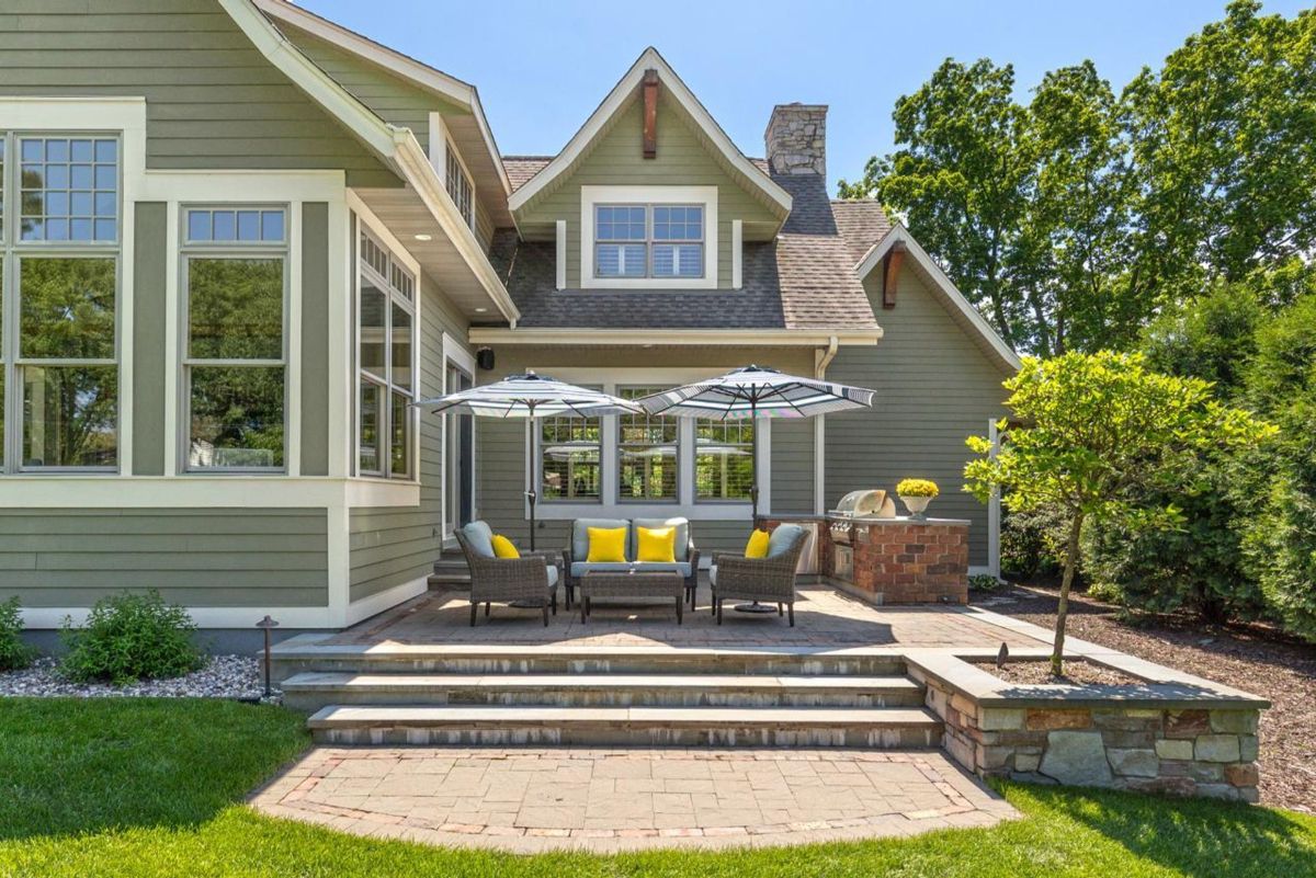 Charming patio space features cozy seating under umbrellas, a built-in grill, and lush landscaping for outdoor gatherings.