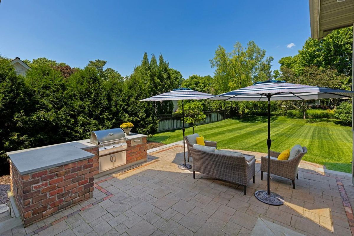 Outdoor patio blends relaxation and entertainment with a built-in brick grill station, shaded seating, and lush greenery.