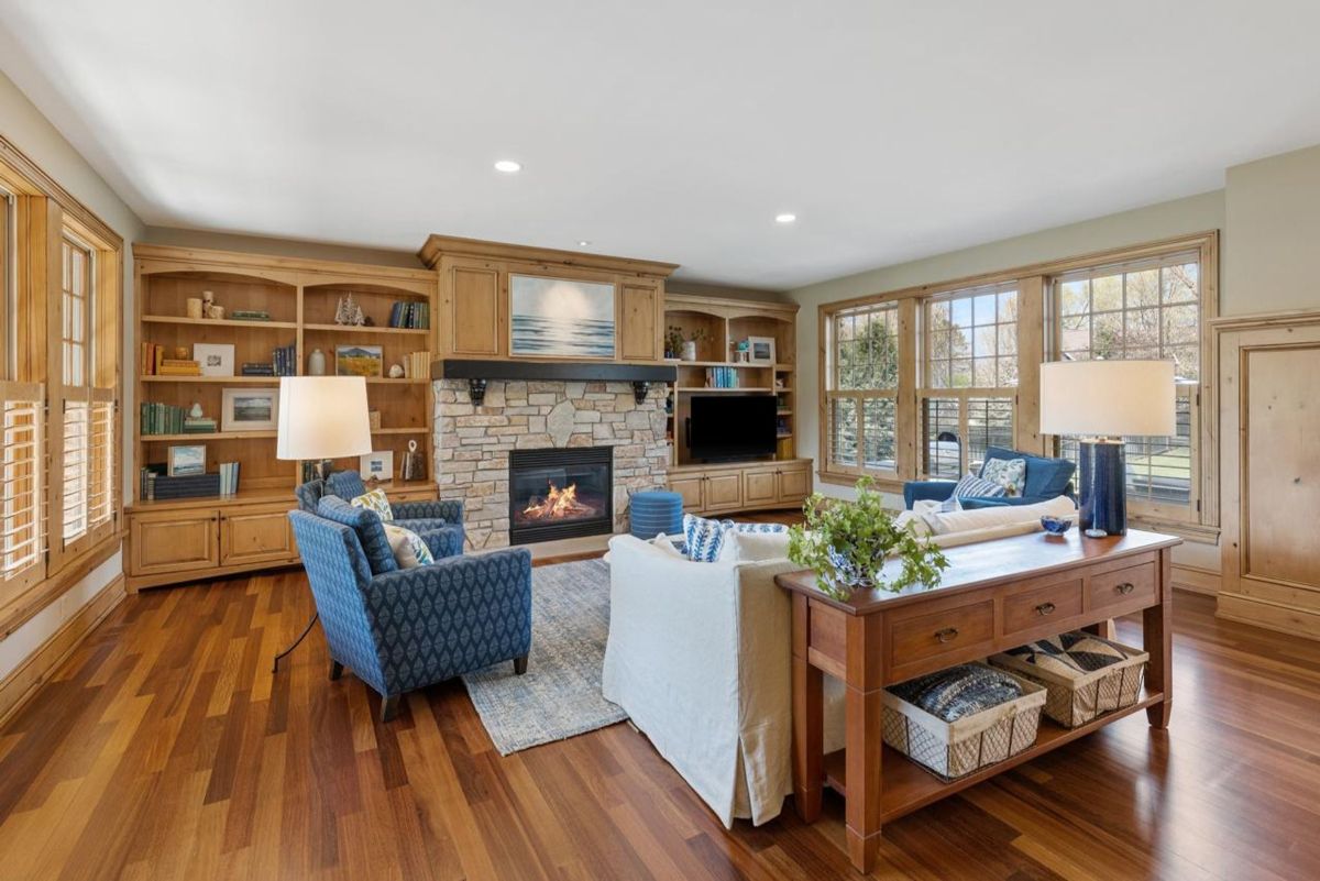 Warm living room features a stone fireplace, custom built-in shelves, and large windows with abundant natural light.