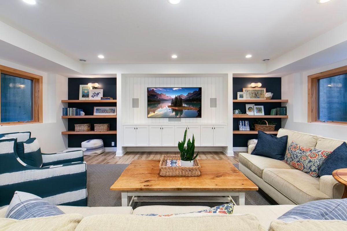 Stylish basement living area combines built-in shelving, cozy seating, and a shiplap entertainment center.