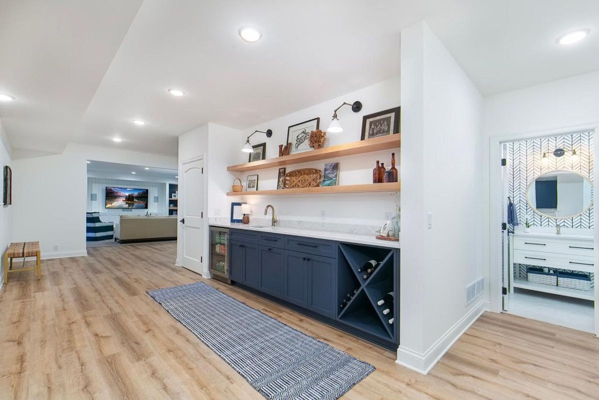 Sleek basement kitchenette features navy cabinetry, open wood shelving, and a built-in wine rack.