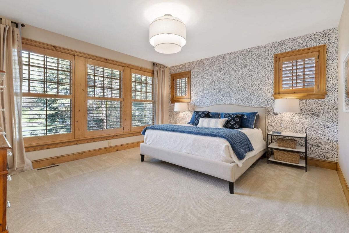 Elegant bedroom combines a patterned accent wall, warm wood shutters, and soothing blue accents.