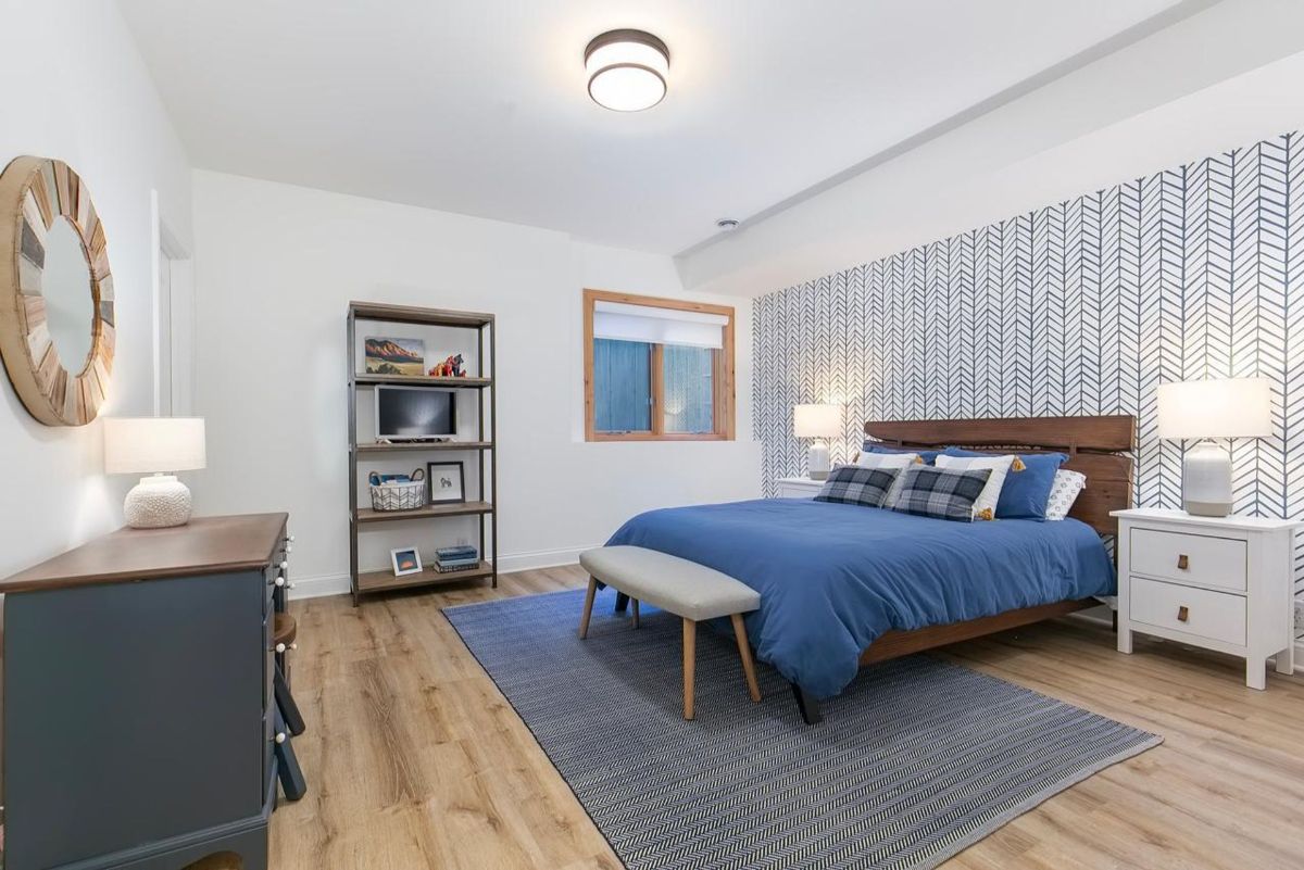 Modern bedroom features bold herringbone accent wall, rich wood furniture, and cozy blue tones.