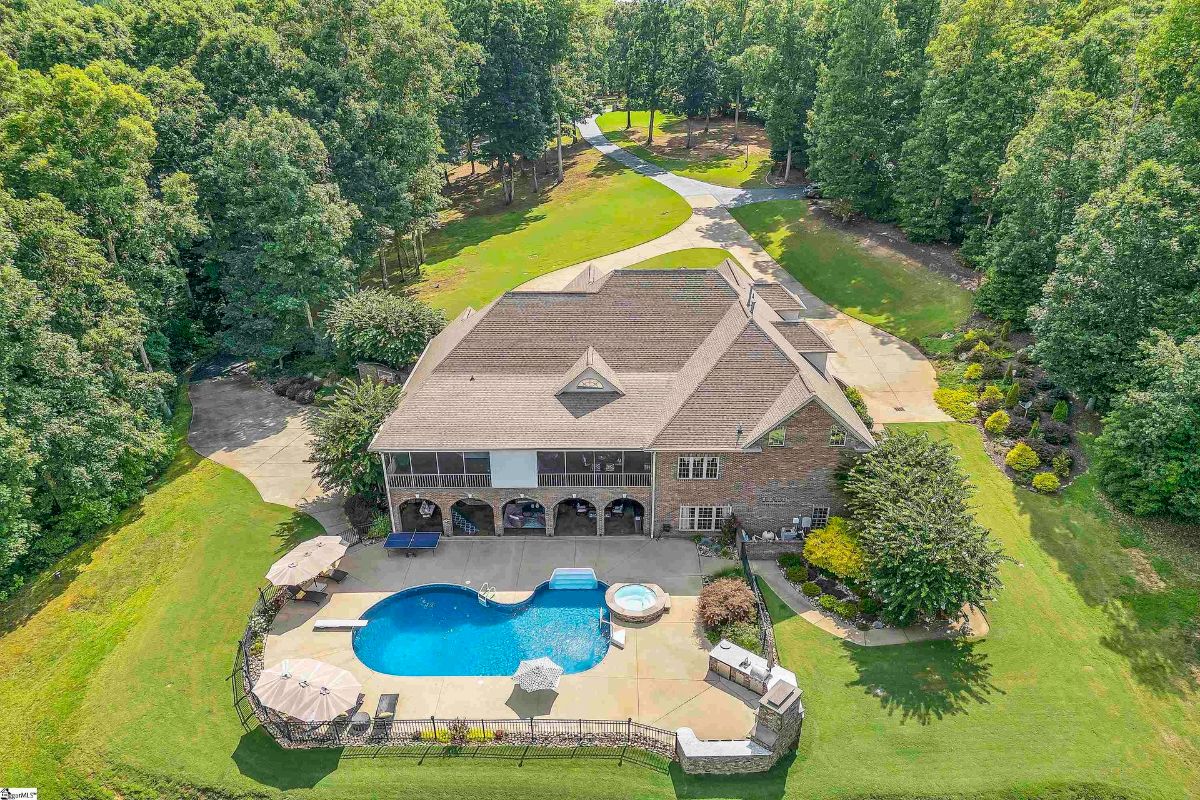 An aerial view reveals a sprawling estate with a custom pool, hot tub, and expansive outdoor entertaining areas surrounded by lush greenery.