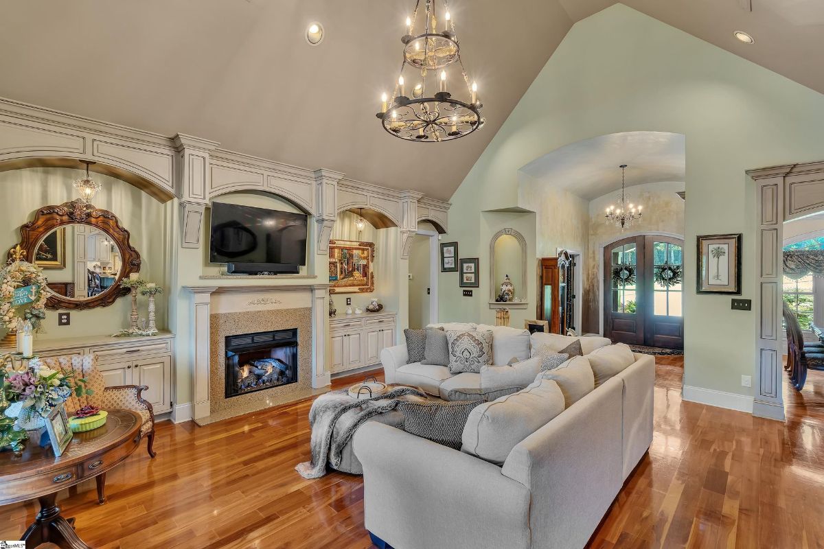 A cozy living area features an arched fireplace, custom built-ins, and elegant moldings, offering a warm and inviting ambiance.