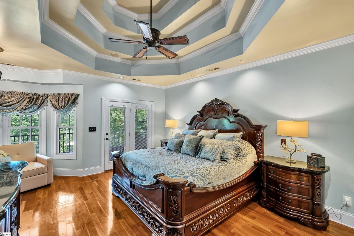 Master suite showcases intricate tray ceilings, elegant furnishings, and access to a private balcony with serene views.