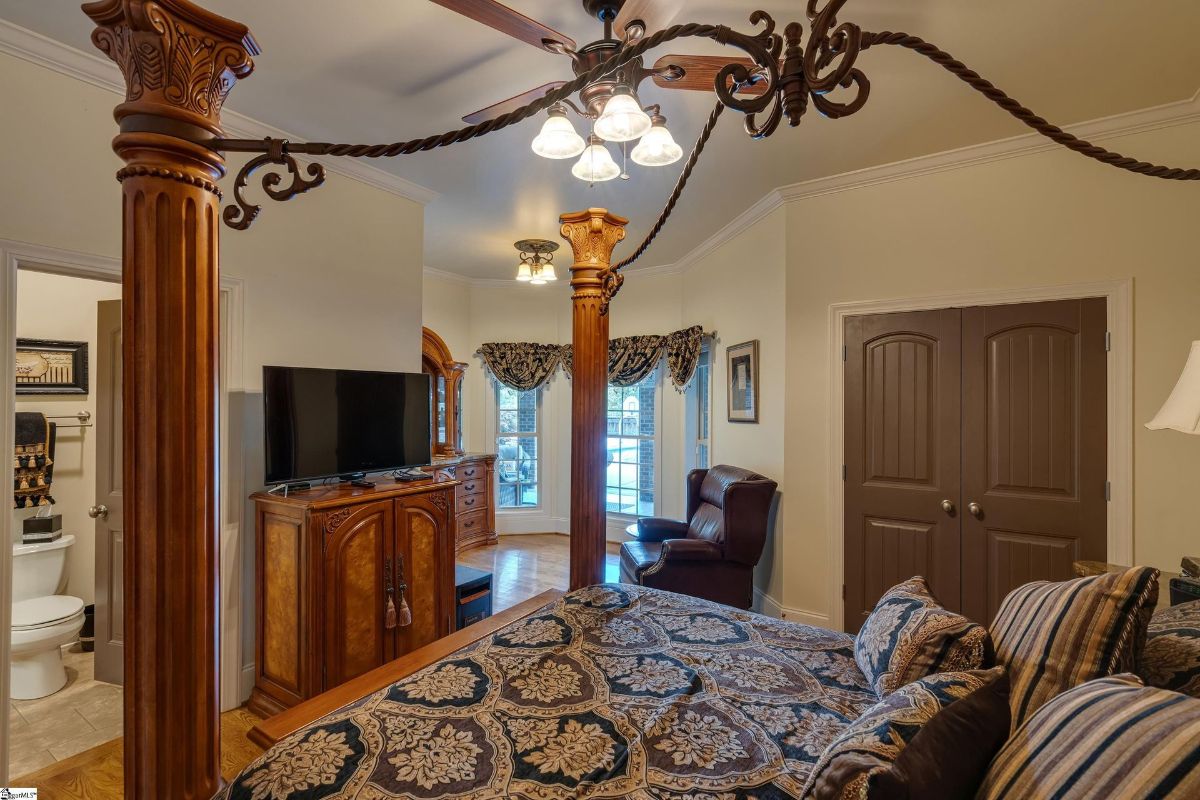 A cozy bedroom exudes charm with ornate furniture, rich textiles, and natural light streaming through large windows.