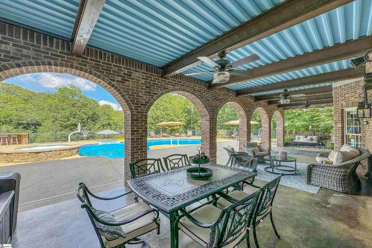 An arched patio with elegant brickwork and ceiling fans overlooks a sparkling pool, creating a perfect spot for outdoor dining and lounging.