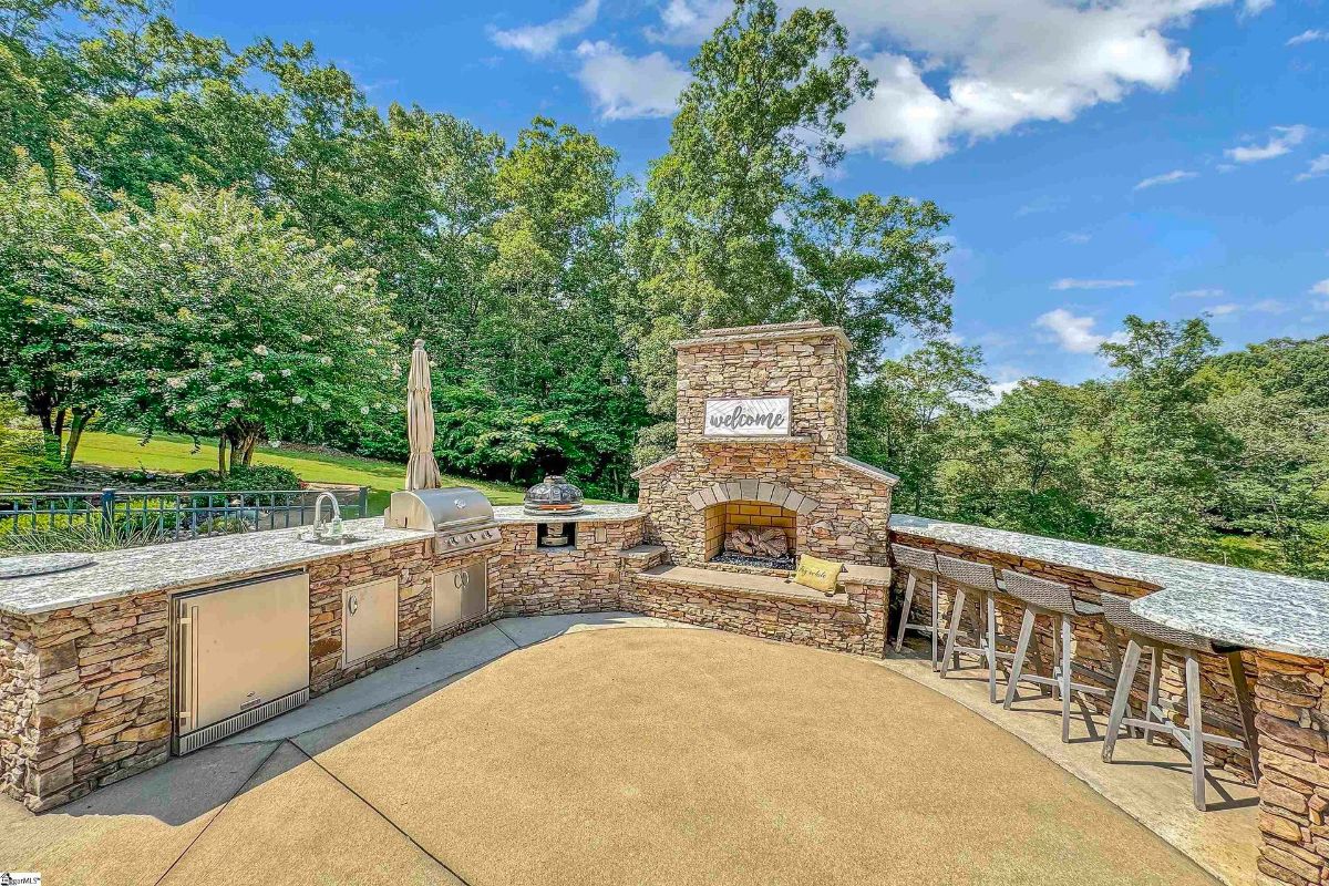 Outdoor kitchen with a built-in grill, stone fireplace, and bar seating creates an inviting space for alfresco dining and entertaining.