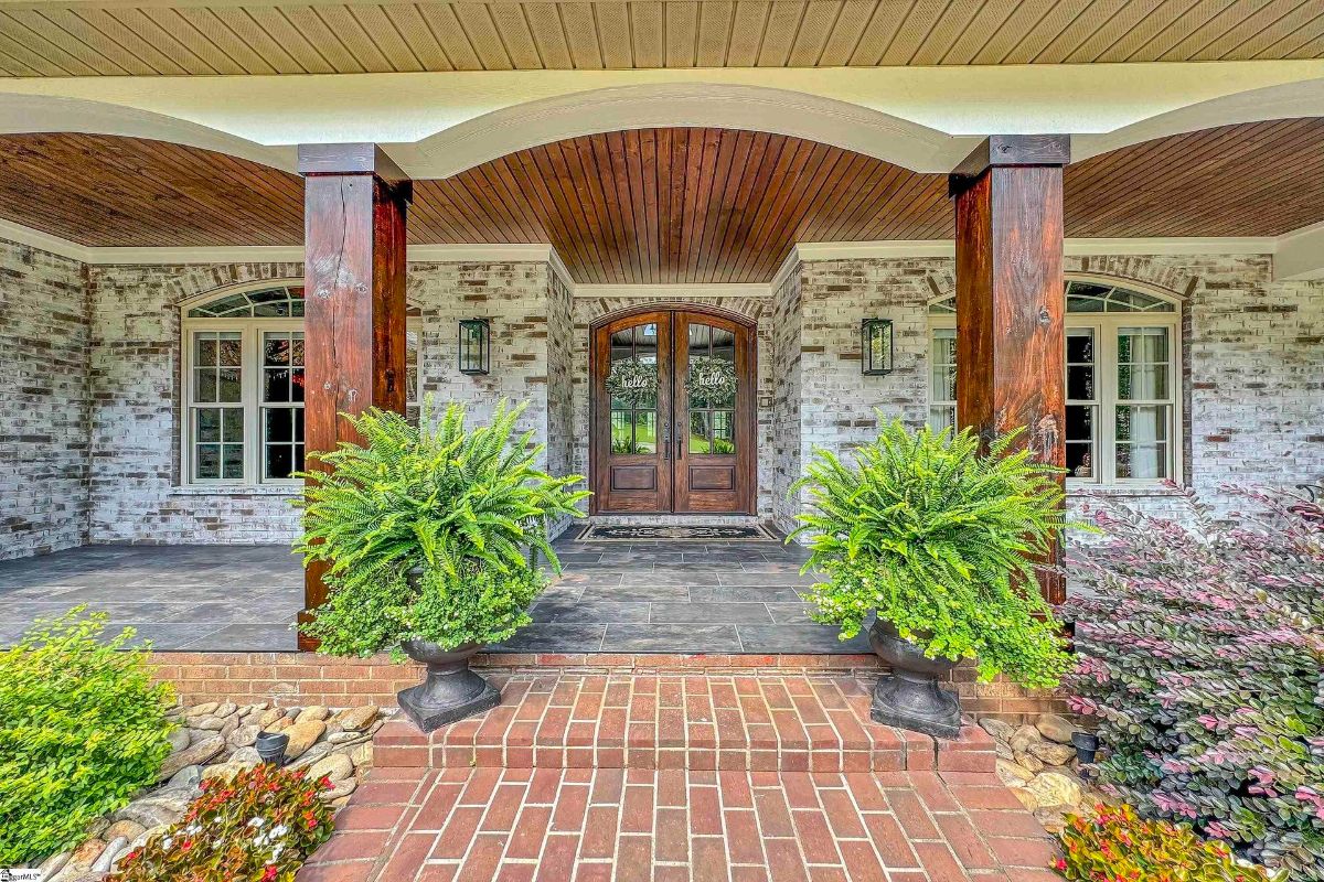 Elegant wooden double doors and brick columns welcome guests to this charming covered porch.