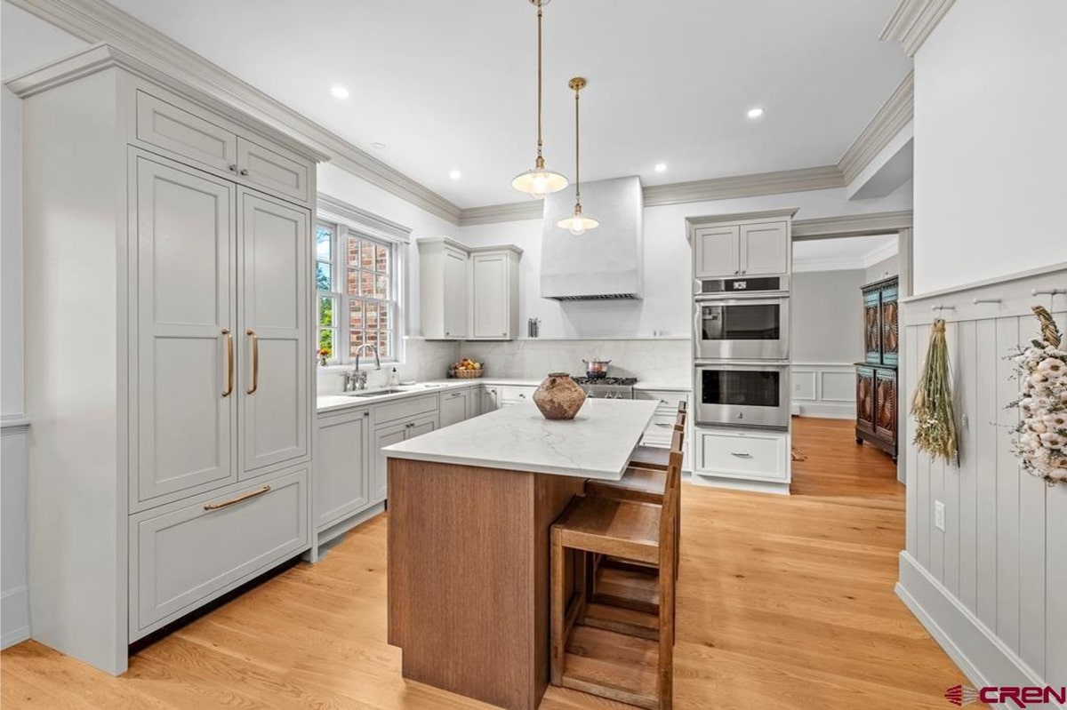 Modern kitchen with light blue cabinets and a light wood kitchen island. There are stainless steel appliances, including a double oven. The kitchen has a bright and airy feel. The floor appears to be hardwood.