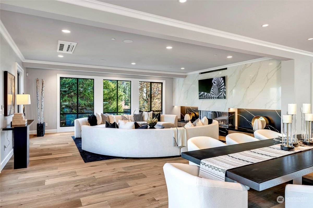 Modern living room with a curved white sectional sofa, a marble fireplace with a zebra artwork above it, and a long, dark dining table with white chairs. 