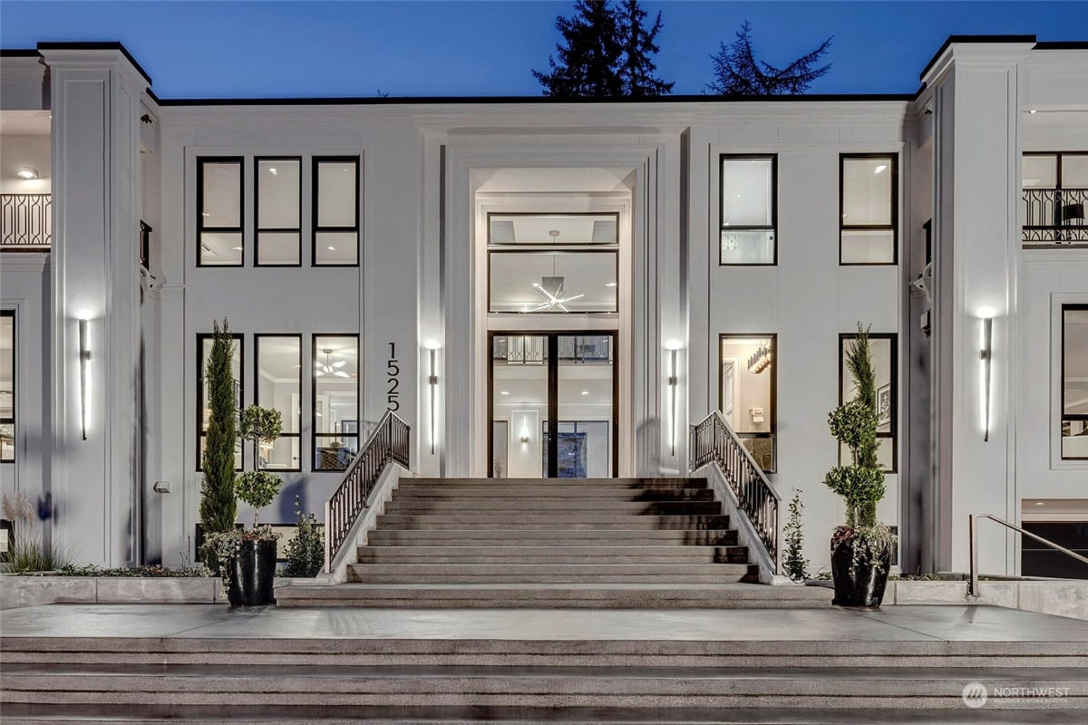 The house is white with black-framed windows and a grand staircase leading to a double glass door entrance.