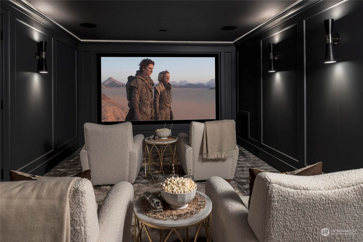 Home theater with dark walls, plush white armchairs, and a large projection screen displaying a landscape scene. 