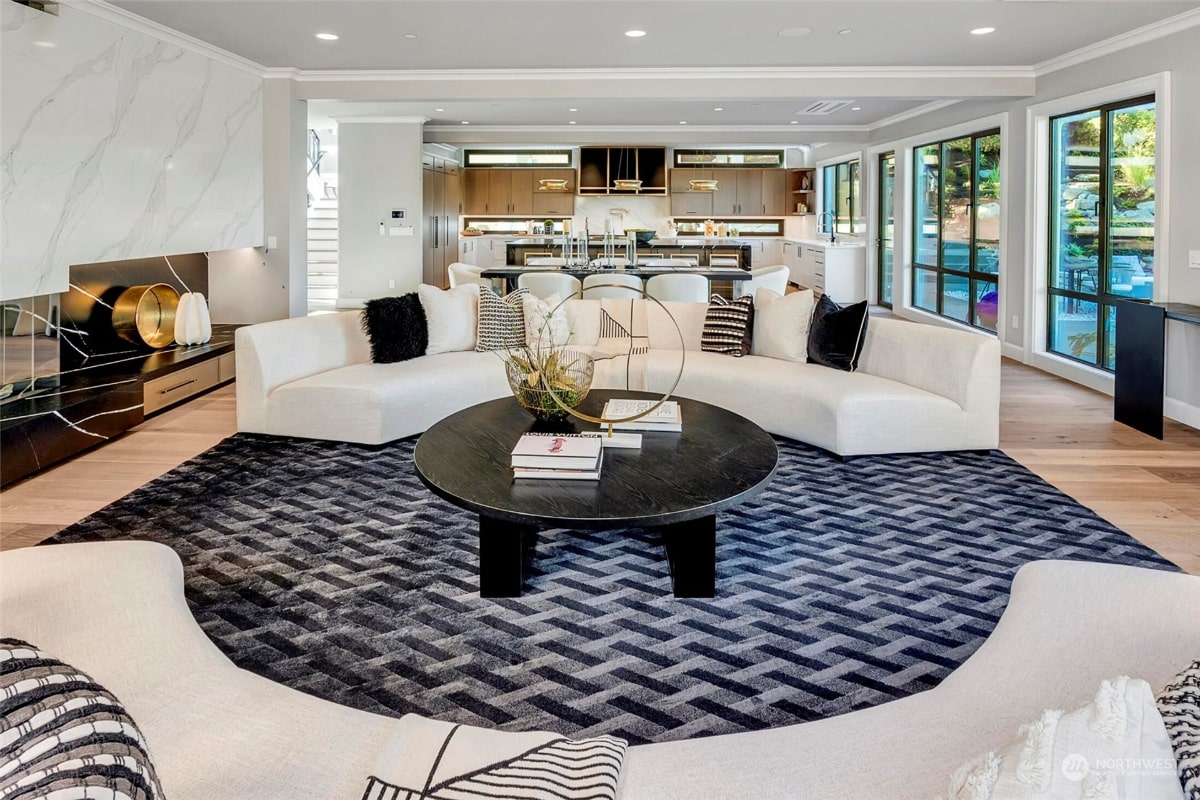 Open-plan living area with a curved white sectional sofa, a dark wood coffee table, and a blue and gray geometric area rug.