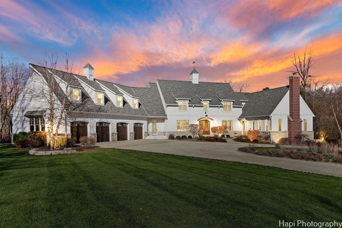 White farmhouse at sunset has a car garage and is surrounded by a well-maintained lawn.