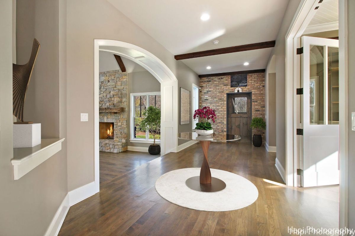 Entryway with hardwood floors, arched doorways, and a stone fireplace is visible through an archway, showcasing a sophisticated and elegant design.