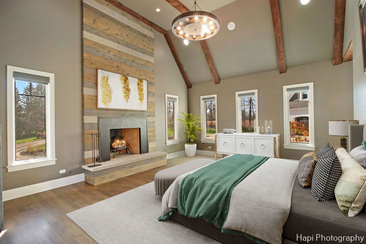 Master bedroom with a wood-paneled fireplace wall, large windows, and a teal-colored bedspread.