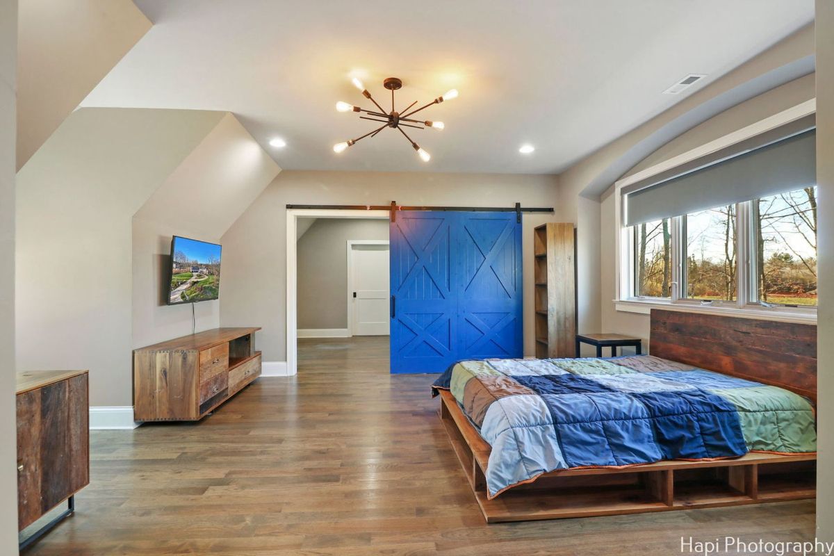 A bedroom with a rustic wooden platform bed, a bright blue barn door, and a modern light fixture features a blend of rustic and contemporary styles.