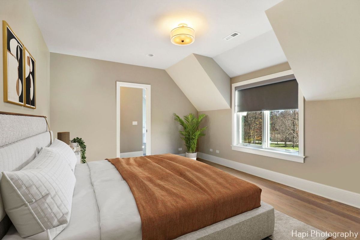 Bedroom with a sloped ceiling, a large window, and a bed with a mauve-colored coverlet offers a tranquil and restful space.