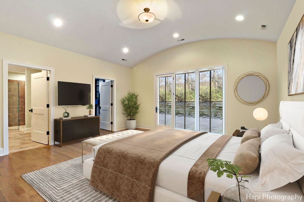 Master bedroom with a vaulted ceiling, large sliding glass doors leading to a patio, and a bed with a mauve-colored throw features a luxurious and relaxing design.