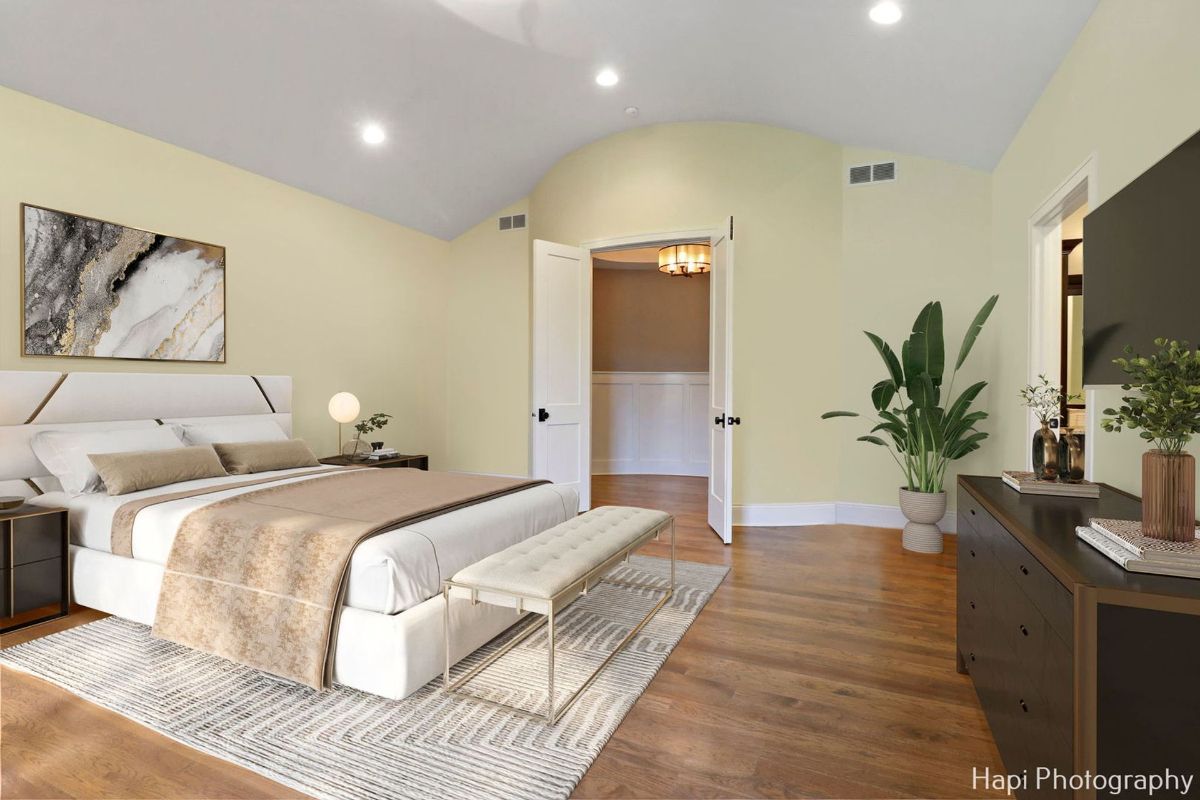 Bedroom with a vaulted ceiling, a large bed with a light beige comforter, and a modern bench features a bright and airy design.