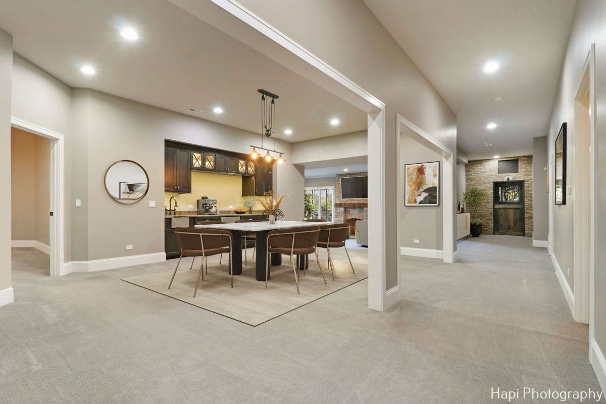 Dining area with a large table, dark brown cabinets, and a contemporary light fixture is situated in an open-plan basement space.