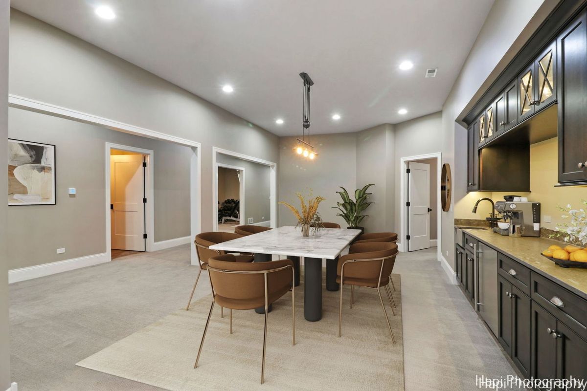 Dining area with a marble table, brown chairs, and a built-in wet bar is situated in a spacious basement. 