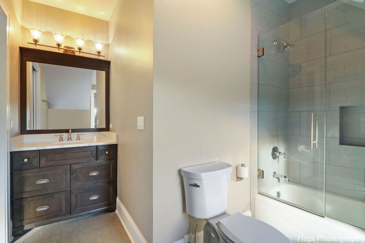 Bathroom with a dark wood vanity, a white toilet, and a walk-in shower with glass doors features a clean and modern design.