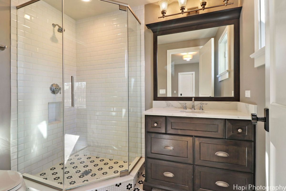 Bathroom with a dark wood vanity, a white subway tile shower with a patterned floor, and a framed mirror showcases a clean and classic design.