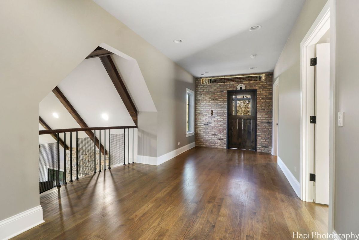 Upper hallway with hardwood floors, an exposed brick wall, and a loft overlook features a unique architectural design.