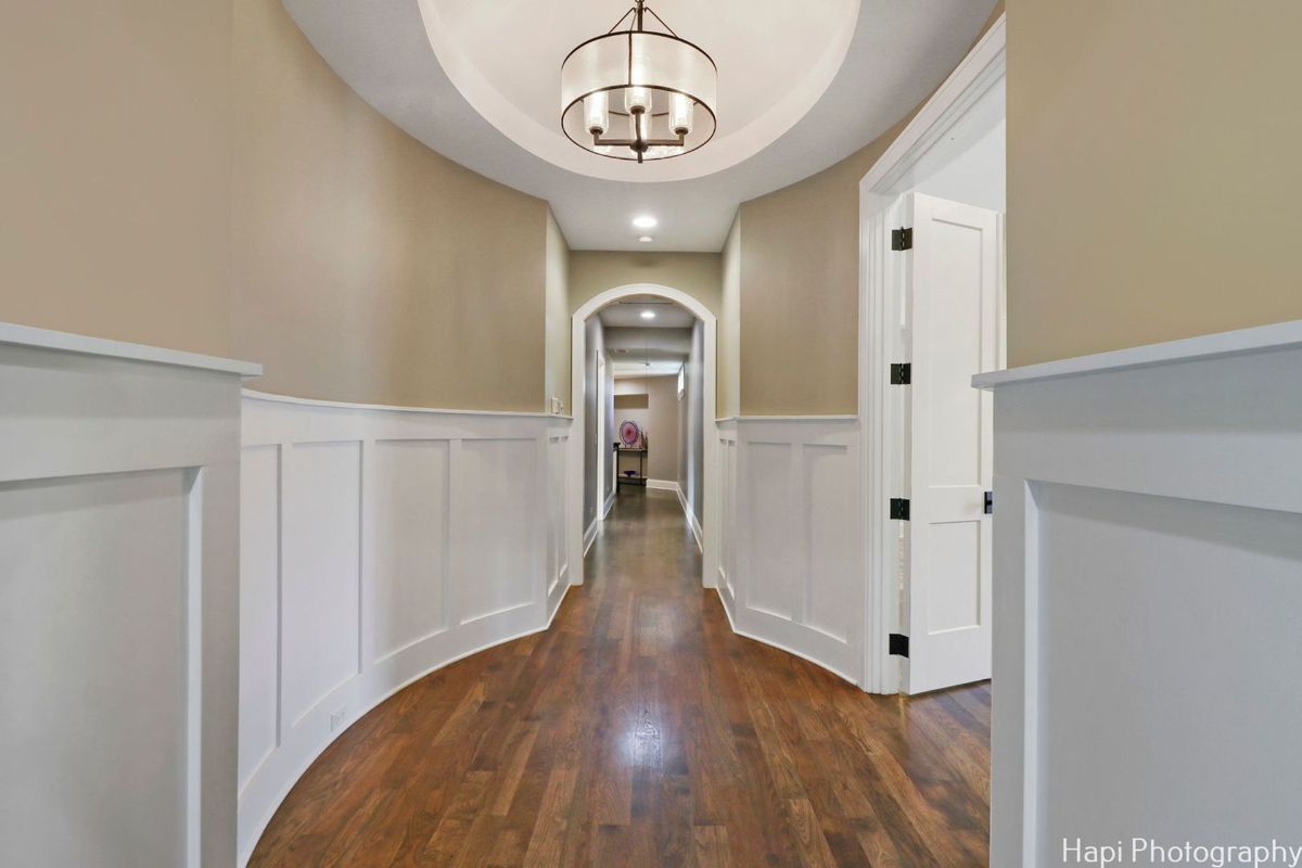 Hallway with hardwood floors, white wainscoting, and a chandelier.