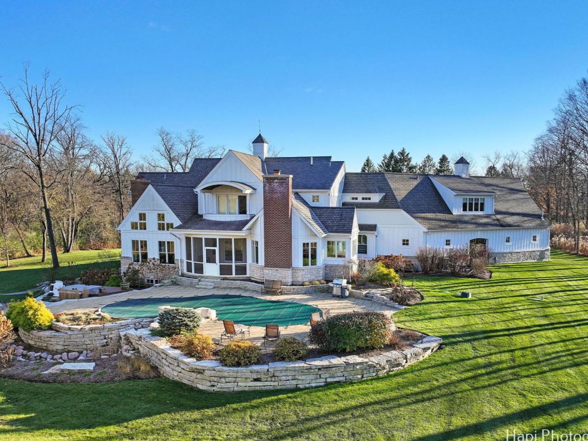 An expansive white farmhouse with a pool and landscaping is captured in an aerial shot.